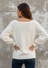 Woman wearing Anya white sweater with sheer sleeves against a beige wall.
