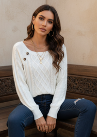 Woman wearing Anya white sweater with button details and blue jeans sitting on a wooden bench.