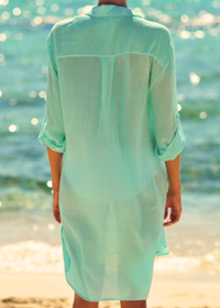 Person wearing a light green dress standing on a beach with ocean in the background