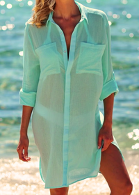 A woman wearing a green Shirt Dress Cover Up, semi-sheer, loose-fit button cover-up, standing by the beach.