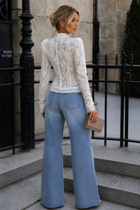 Woman wearing a lace top and blue jeans standing on steps outdoors.