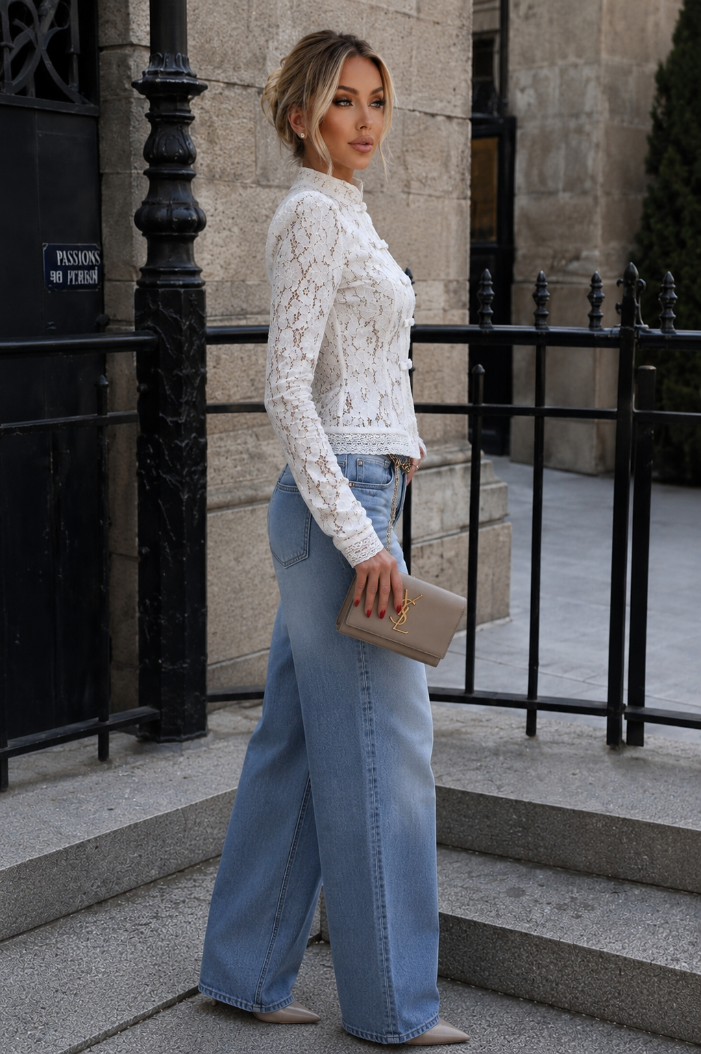 Woman in white lace top and blue jeans standing outdoors near a building.
