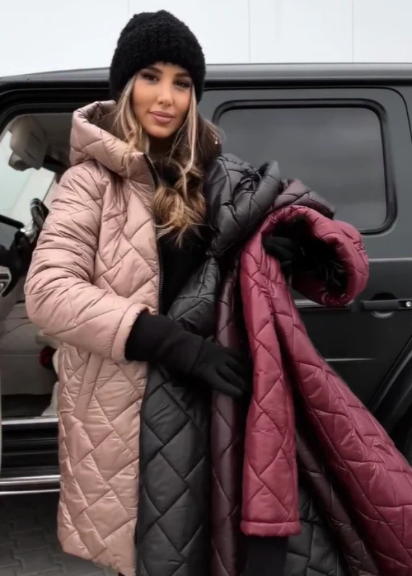 Woman holding three quilted coats in front of a car