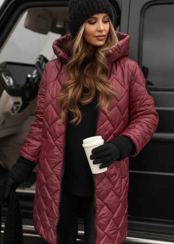 Woman in a long quilted pink coat holding a coffee cup, standing next to a vehicle.