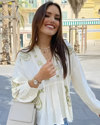 Woman wearing a VV white embroidered top with green patterns outdoors.