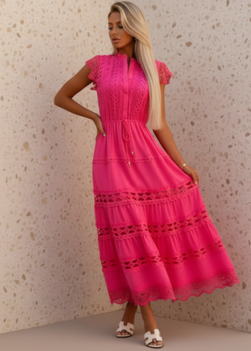 Woman wearing a bright pink dress with lace details against a textured beige wall.