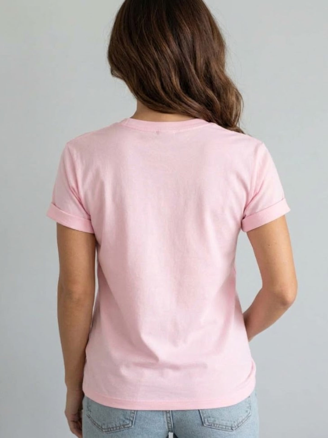 A woman viewed from behind wearing a Villa Vibes Designer Inspired light pink short-sleeve t-shirt and light blue jeans against a plain light gray background.