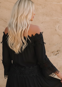 Woman in a black Diaz dress  against a stone wall.
