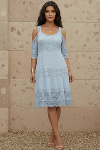 Woman wearing Ella light blue lace dress against a beige wall.
