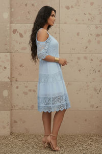 Woman wearing Ella light blue lace dress against a beige wall.