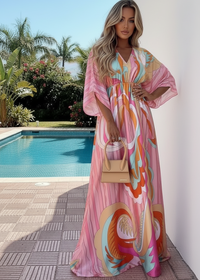 Woman in a colorful Enya Kaftan dress standing by a pool with palm trees in the background