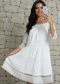 Woman in a white Fallon dress taking a selfie against a stone wall.