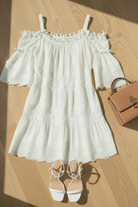 Villa Vibes Fallon White off-shoulder dress with ruffled details, white sandals, and a brown handbag on a wooden floor.