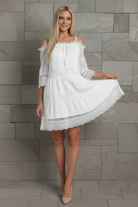 Woman wearing a white fallon dress with lace details against a stone wall.