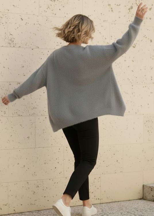 Person wearing aZendaya gray sweater and black pants against a textured wall.