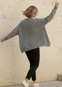 Person wearing aZendaya gray sweater and black pants against a textured wall.