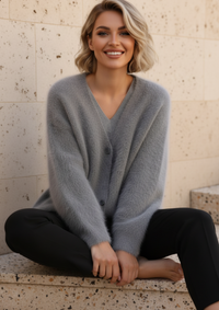 Woman wearing Zendaya gray cardigan sitting on steps with a light-colored wall background