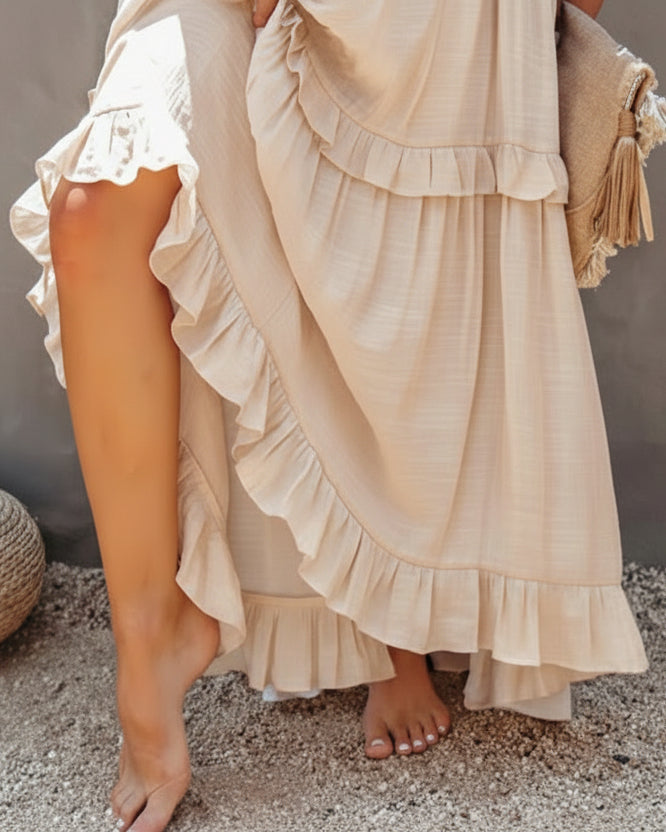 Woman wearing a flowing beige dress with ruffles on a textured surface.