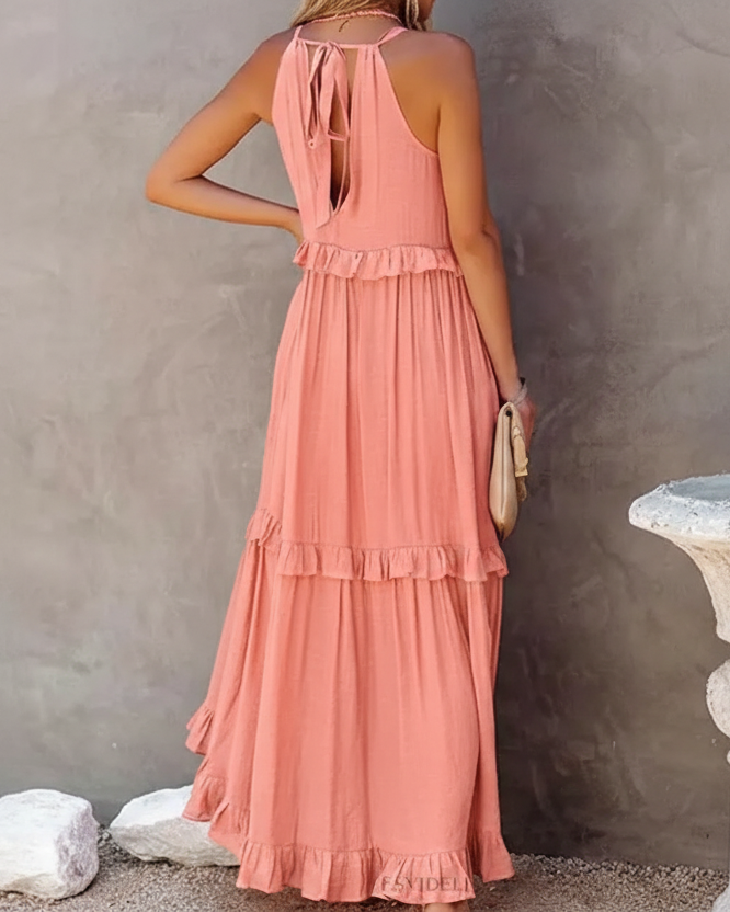 Woman in a long pink dress standing next to a stone pedestal against a plain wall.