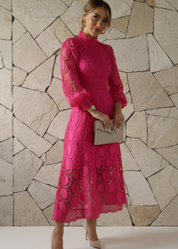 Woman wearing a pink lace dress against a stone wall.