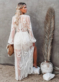 Woman in a white lace dress standing against a gray wall with decorative elements.