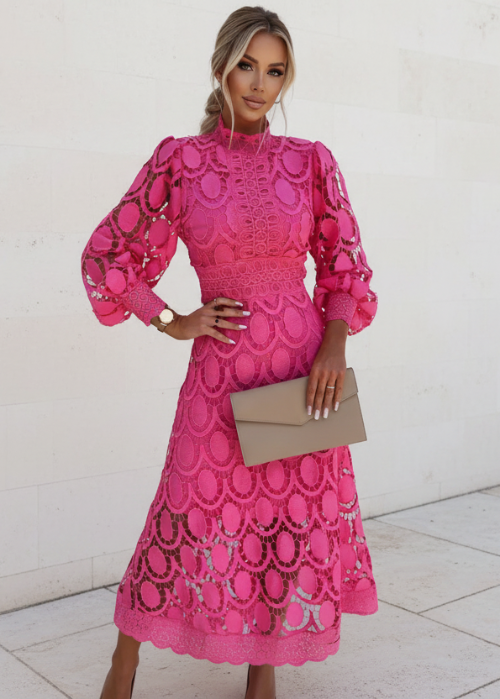 Woman wearing a pink lace dress holding a beige clutch against a white background