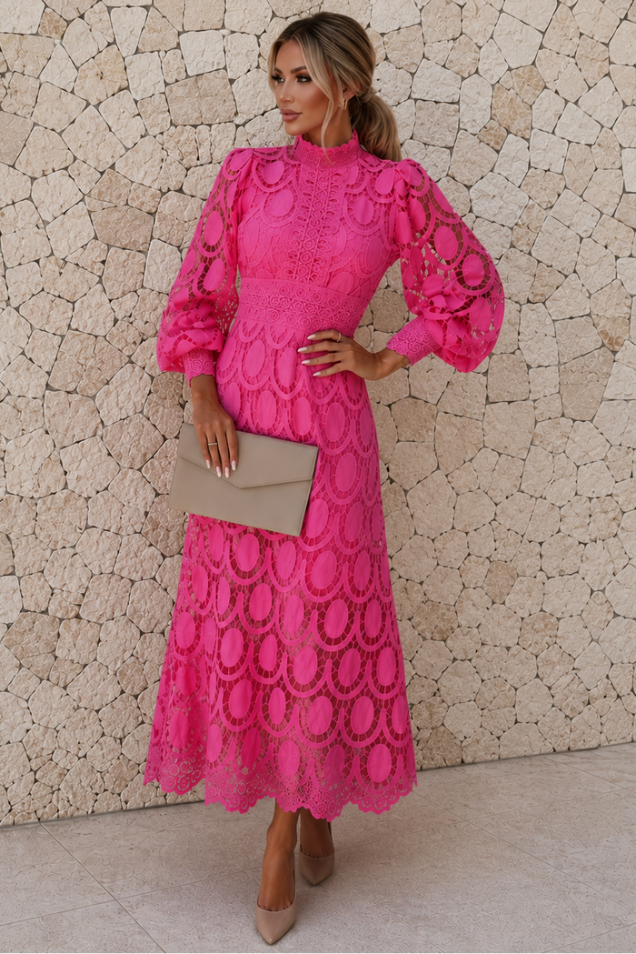 Woman wearing a pink Jasmine lace dress against a stone wall.