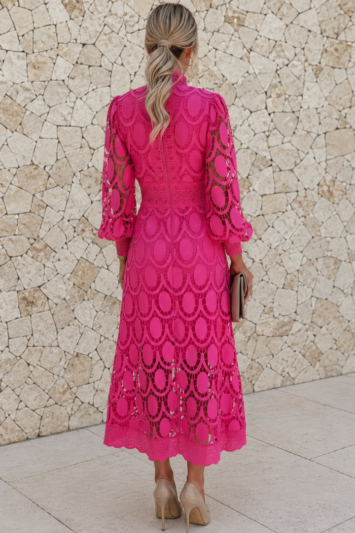 Woman wearing a bright pink Jasmine dress with a geometric pattern, standing against a stone wall.