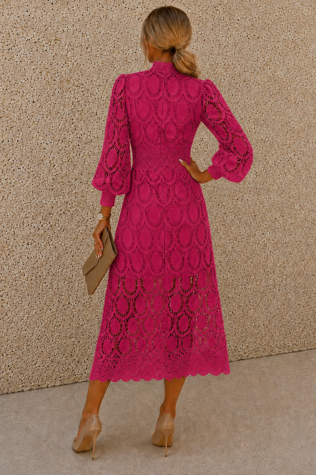 A woman shown from the back wearing a bright pink lace midi dress with long balloon sleeves and a high neckline, standing against a textured beige wall.