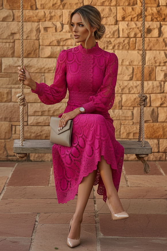 A woman wearing a bright fuchsia pink lace midi dress with a high-low hem sits on a rope swing in front of a stone wall. She is holding a taupe clutch and wearing beige heels.