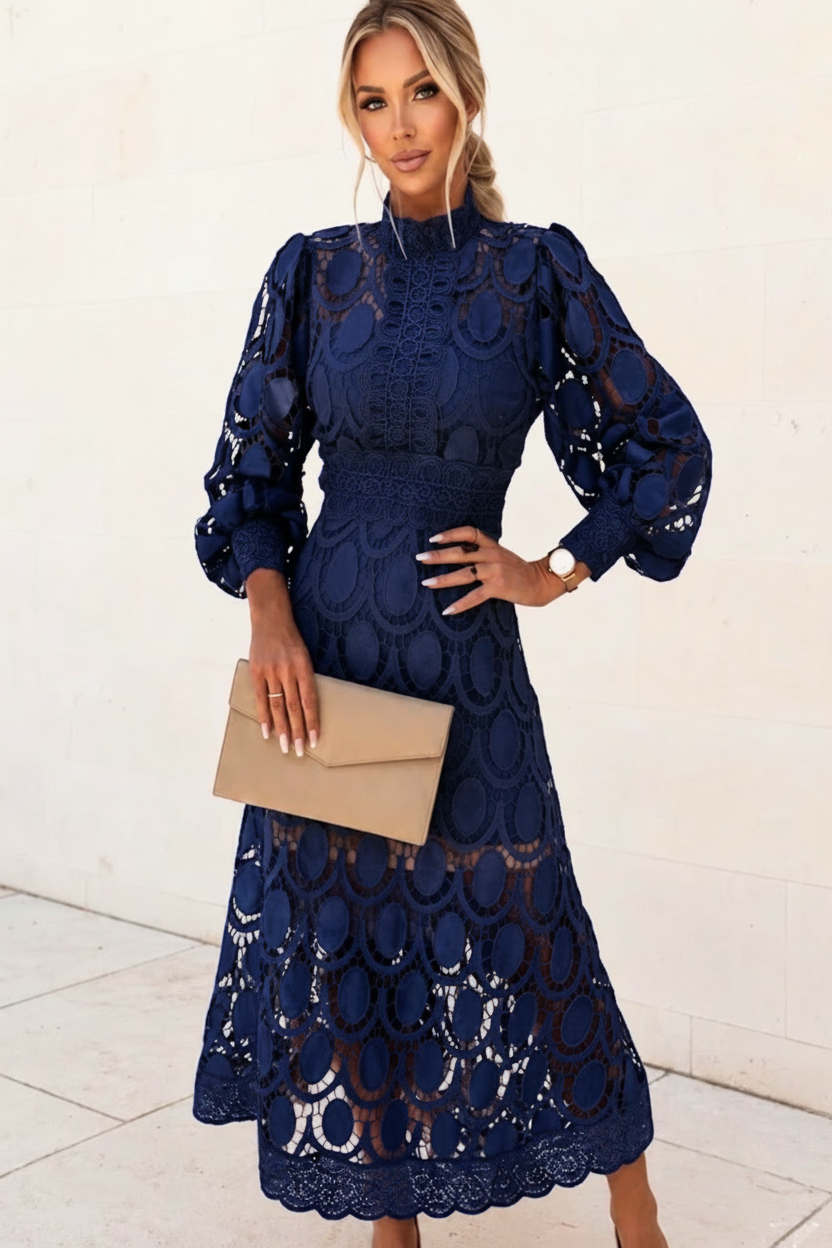 Woman wearing a Jasmine blue lace dress holding a beige clutch against a white background