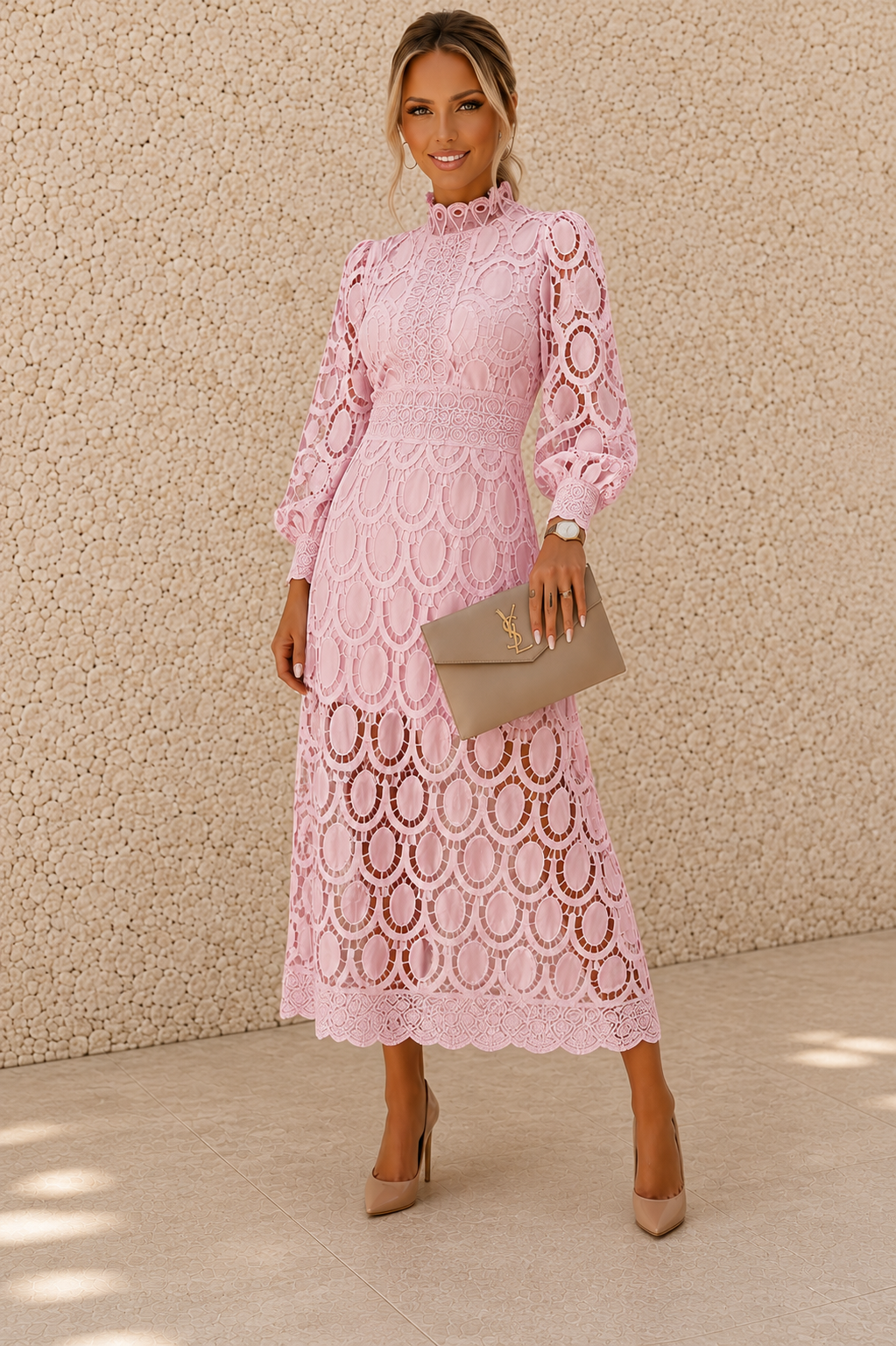 A woman models a light pink long-sleeve lace midi dress with a high ruffled collar and an allover circular lace pattern. She is holding a taupe clutch and wearing nude heels, standing against a textured beige stucco wall.