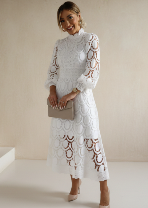 Woman wearing a white lace dress with long sleeves against a plain background