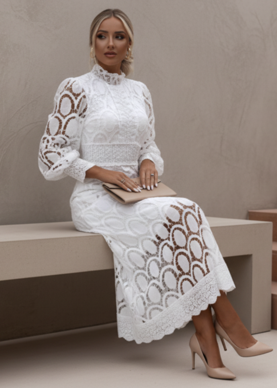 Woman wearing a Jasmine white lace dress sitting on a bench.
