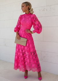 Woman wearing a bright pink lace dress against a white wall.