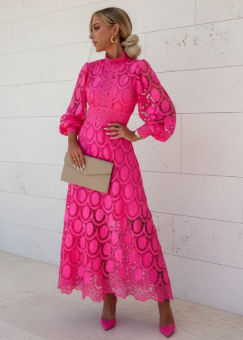Woman wearing a bright pink lace dress against a white wall.
