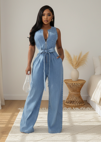 Woman wearing Karina blue denim jumpsuit in a room with a white wall and wooden floor.