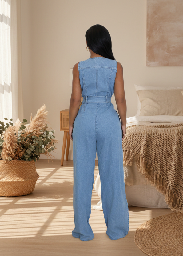 Woman wearing Karina blue denim jumpsuit in a cozy room with a bed and decorative plants.