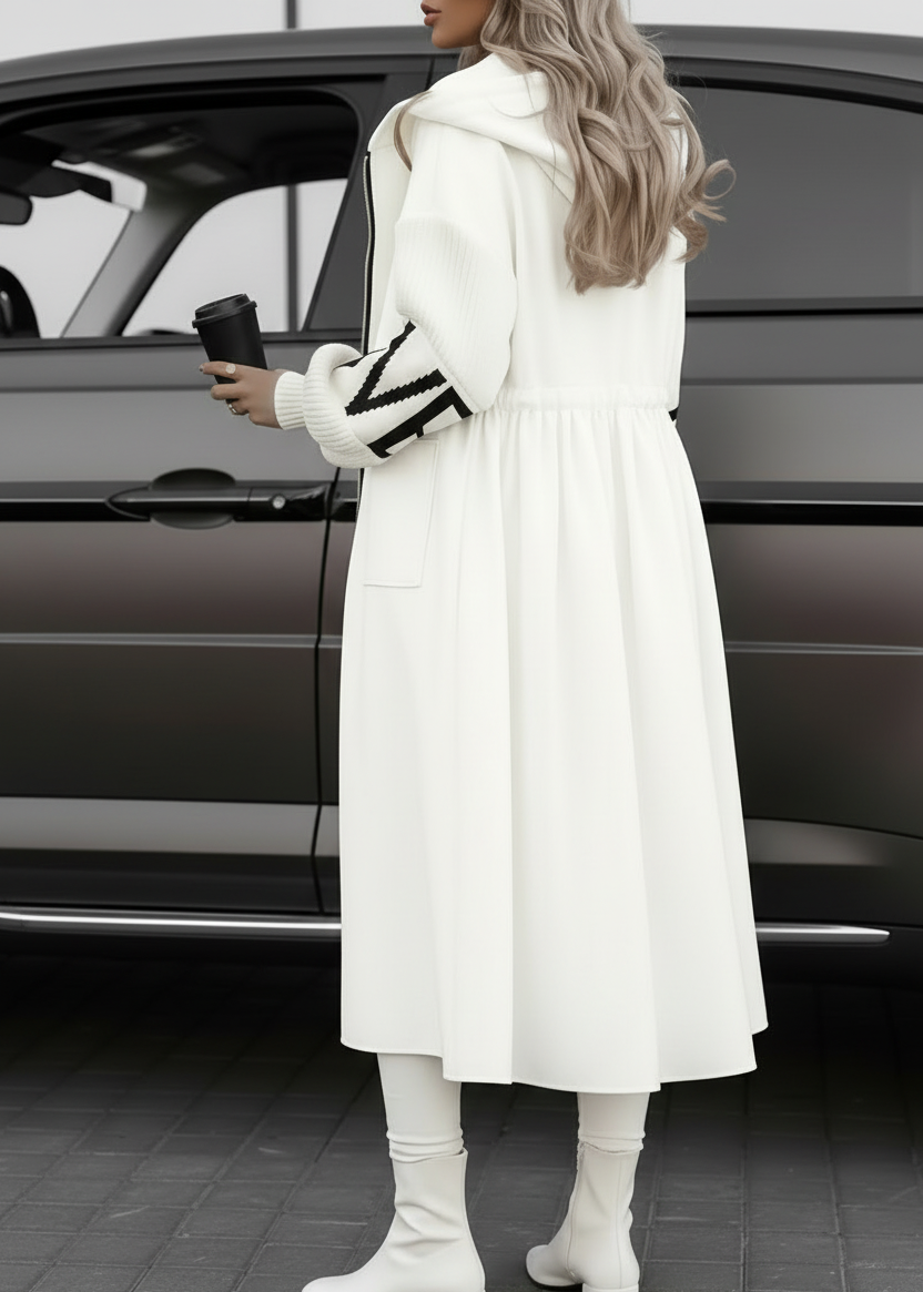 Person wearing Kelly long white coat with black and white gloves, standing next to a car.