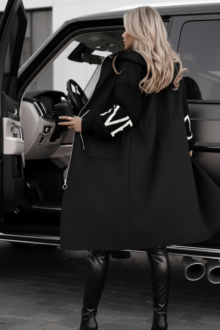 Woman in a black Kelly coat with white lettering getting out of a car.