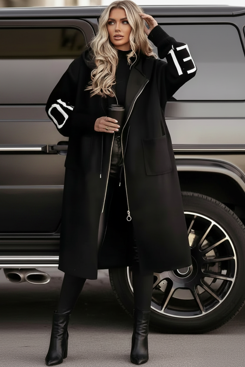 Woman in a black Kelly coat with white text standing next to a car