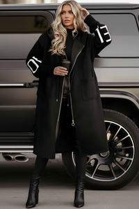Woman in a black Kelly coat with white text standing next to a car