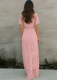 Woman wearing Lotus pink lace dress standing against a plain wall.