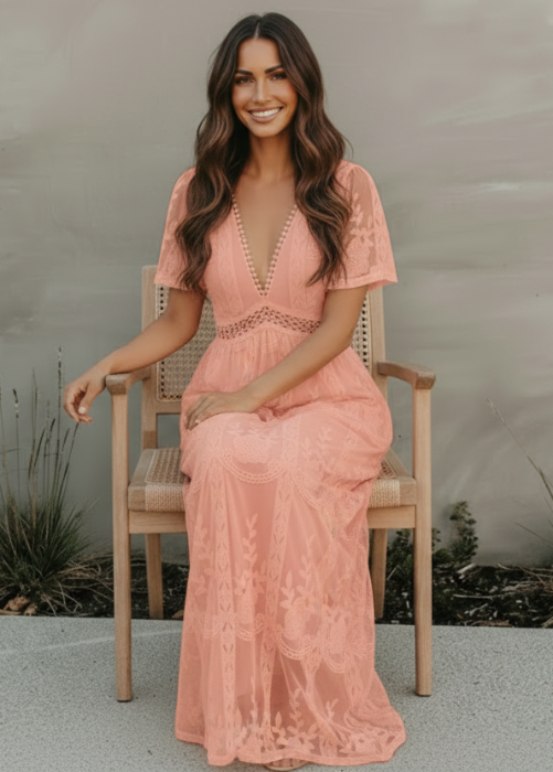 Woman in a pink lace dress sitting on a chair outdoors.