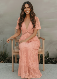 Woman in a pink lace dress sitting on a chair outdoors.
