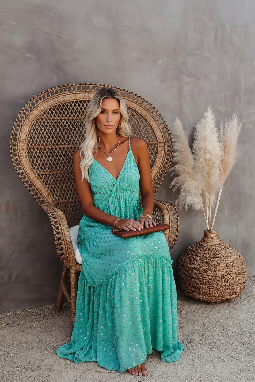 Woman in a teal dress standing next to a textured wall and decorative plant.
