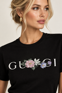 A close-up of a woman wearing a black crewneck t-shirt with a floral embroidered design and the word 'GU8CI' in white across the chest.