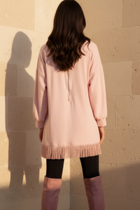 Woman wearing Maddox pink dress and black knee-high boots against a beige stone wall.