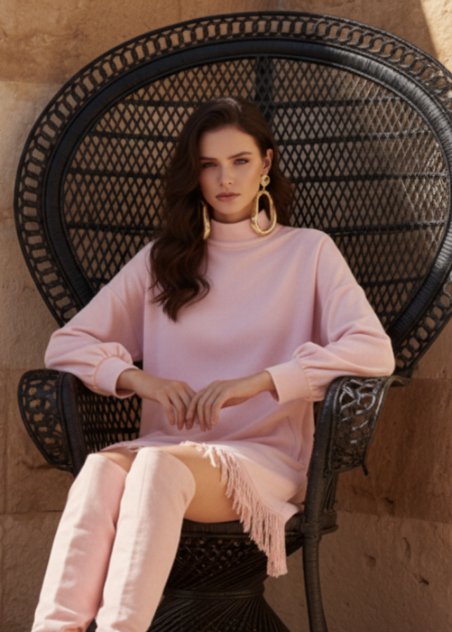 Woman in Maddox pink dress and matching knee-high boots sitting on a black wicker chair.