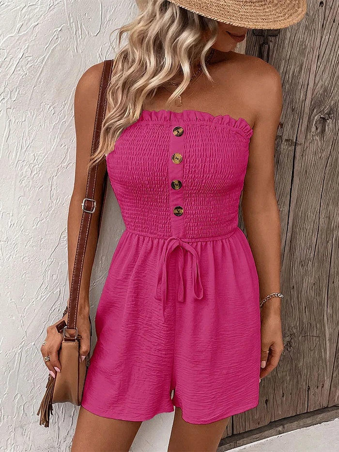 Woman wearing a pink Paige strapless romper with buttons against a textured wall.